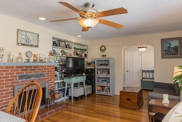 living room featuring ceiling fan, hardwood / wood-style flooring, a fireplace, and built in shelves