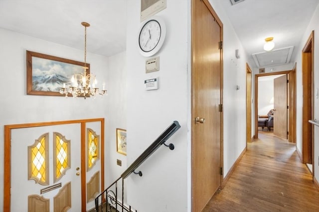 hall featuring an inviting chandelier, attic access, wood finished floors, and an upstairs landing