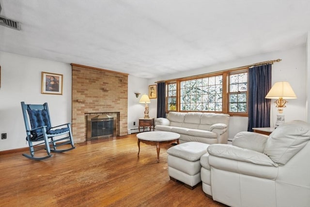 living area featuring a brick fireplace, visible vents, baseboard heating, and wood finished floors