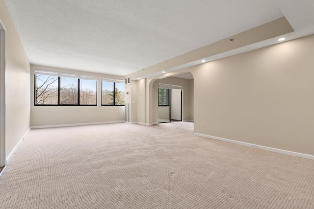 spare room featuring arched walkways, recessed lighting, baseboards, and light colored carpet