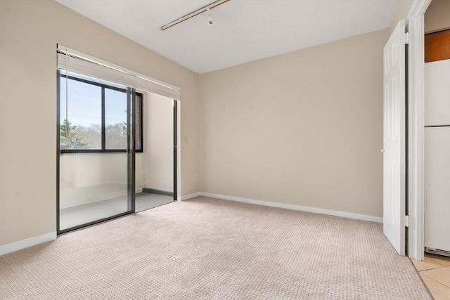 spare room featuring light carpet, rail lighting, and baseboards