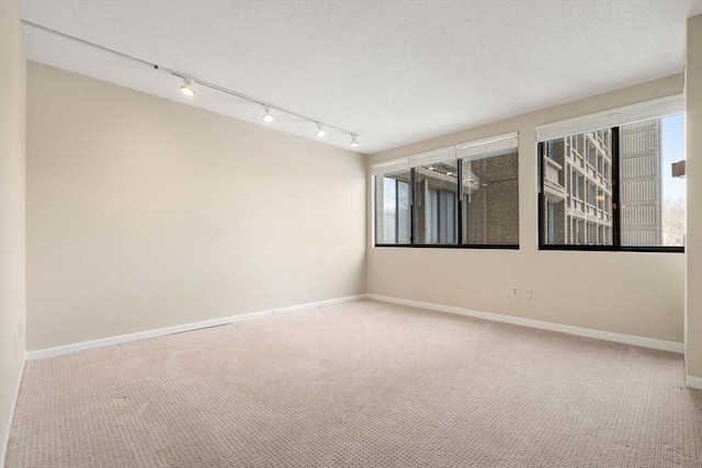 carpeted spare room featuring a textured ceiling, baseboards, and track lighting