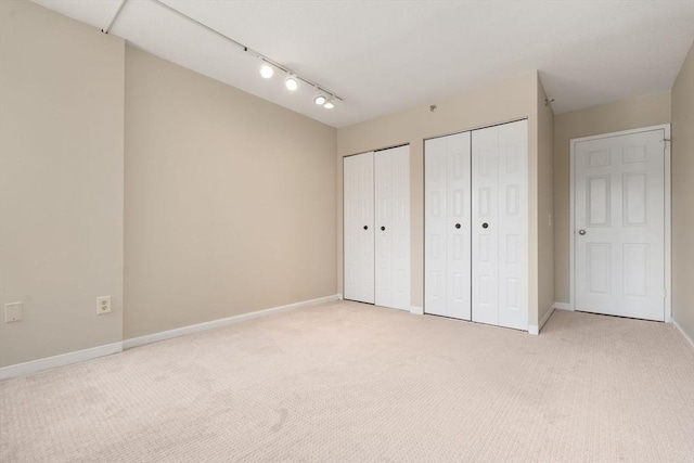 unfurnished bedroom with light carpet, baseboards, and multiple closets