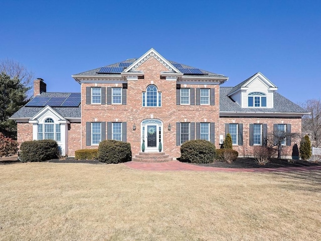 view of front of home featuring solar panels, brick siding, and a front yard