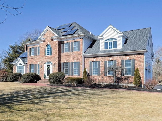 view of front of property featuring solar panels, a front lawn, a shingled roof, and brick siding