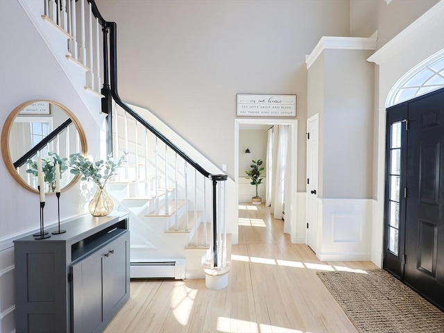 foyer featuring a towering ceiling, a baseboard radiator, stairway, and light wood-style flooring