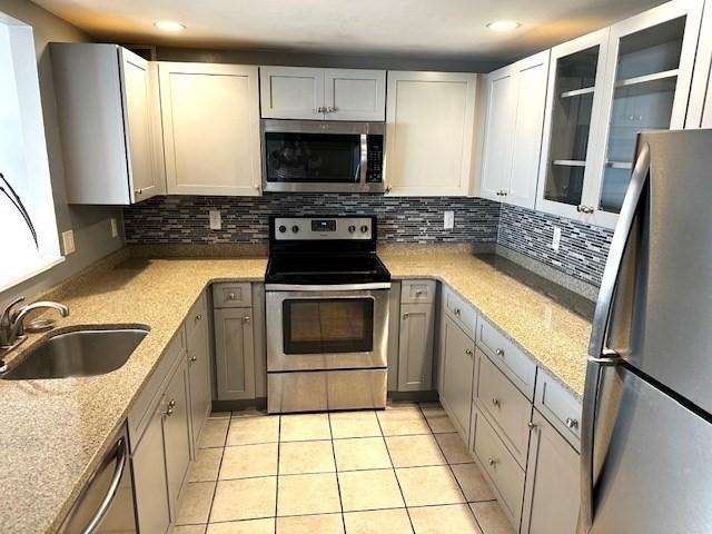 77 Adams St Unit 1201, Quincy, MA 02169 - kitchen with stainless steel appliances, a sink, decorative backsplash, light tile patterned floors, and light stone counters