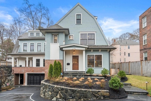 shingle-style home featuring brick siding, an attached garage, fence, and aphalt driveway