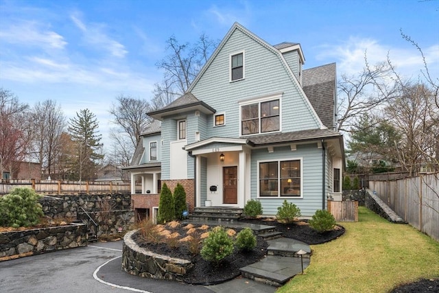 shingle-style home with roof with shingles, a gambrel roof, fence, and a front lawn