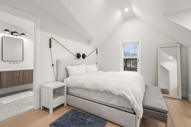 bedroom with light wood-type flooring, vaulted ceiling, and connected bathroom