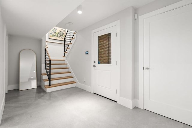entrance foyer featuring concrete floors, baseboards, and stairway