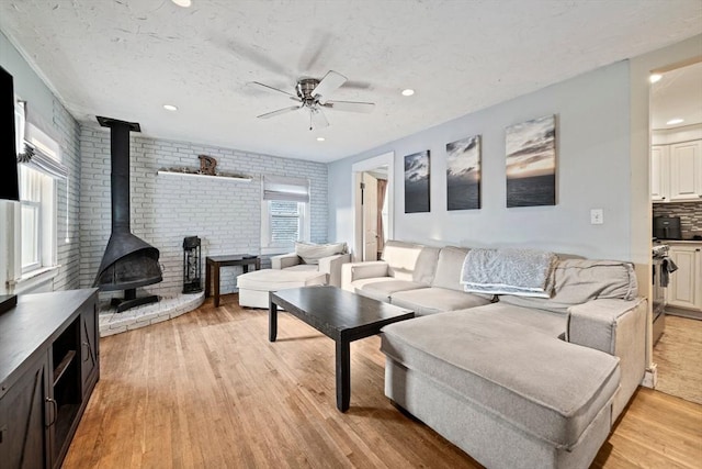 19 Borden, Scituate, MA 02066 - living area featuring a wood stove, light wood-style floors, ceiling fan, brick wall, and a textured ceiling