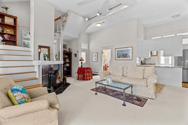 carpeted living room featuring a towering ceiling, a fireplace, a healthy amount of sunlight, and baseboard heating