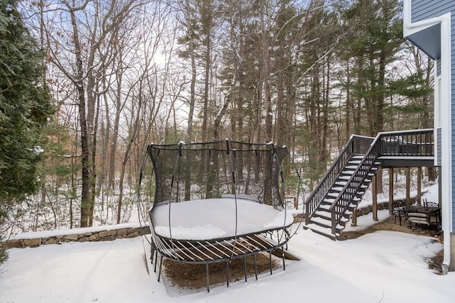 yard layered in snow with a trampoline and a wooden deck