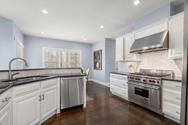 kitchen with appliances with stainless steel finishes, sink, dark stone counters, wall chimney exhaust hood, and white cabinets