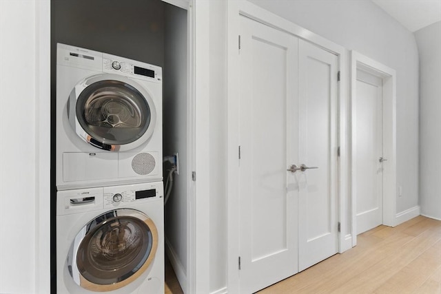 clothes washing area featuring stacked washer / drying machine, light wood finished floors, and baseboards