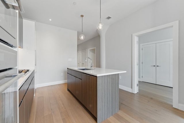 kitchen featuring modern cabinets, a sink, light wood-type flooring, light countertops, and pendant lighting