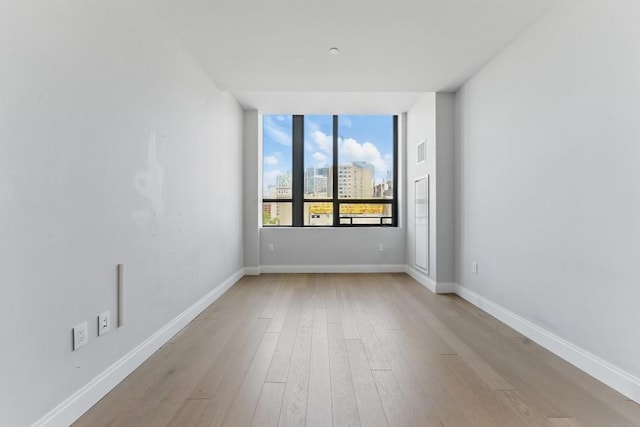 empty room featuring light wood-type flooring, baseboards, and a city view