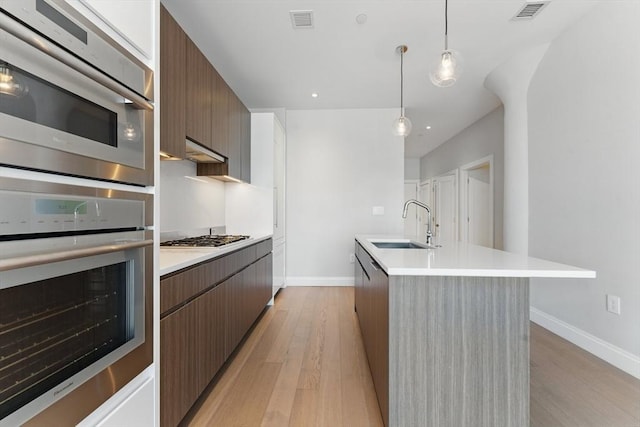 kitchen featuring stainless steel appliances, modern cabinets, a sink, baseboards, and light countertops