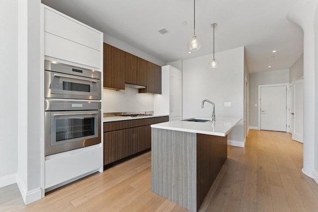 kitchen with a sink, stainless steel double oven, modern cabinets, light countertops, and gas stovetop