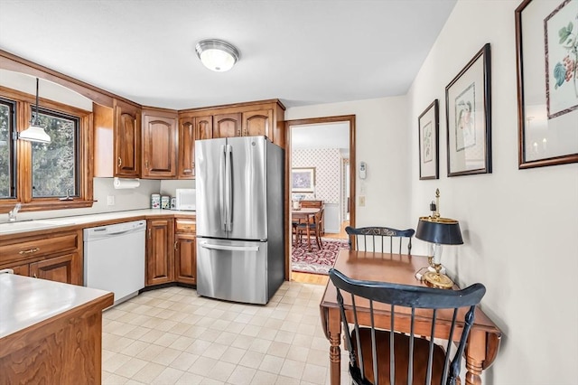 kitchen featuring white appliances, a sink, light countertops, brown cabinetry, and decorative light fixtures