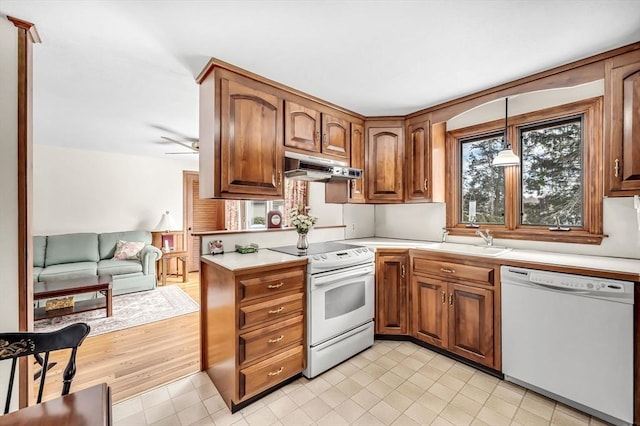 kitchen featuring brown cabinets, decorative light fixtures, light countertops, white appliances, and under cabinet range hood