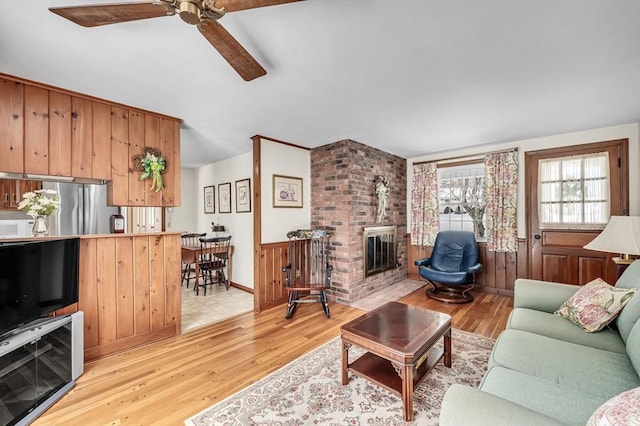 living room featuring wine cooler, a brick fireplace, ceiling fan, and light wood finished floors