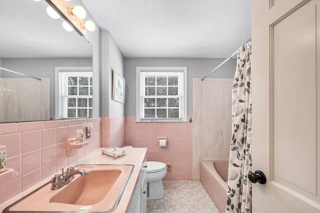 full bathroom featuring toilet, tile walls, vanity, wainscoting, and shower / tub combo with curtain