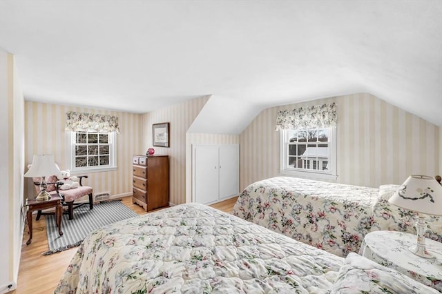 bedroom featuring vaulted ceiling, light wood-type flooring, and wallpapered walls