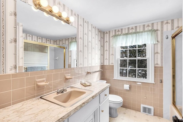 bathroom with toilet, a wainscoted wall, vanity, visible vents, and wallpapered walls