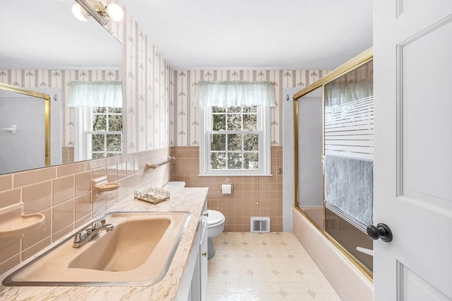 full bathroom with toilet, vanity, visible vents, combined bath / shower with glass door, and wallpapered walls