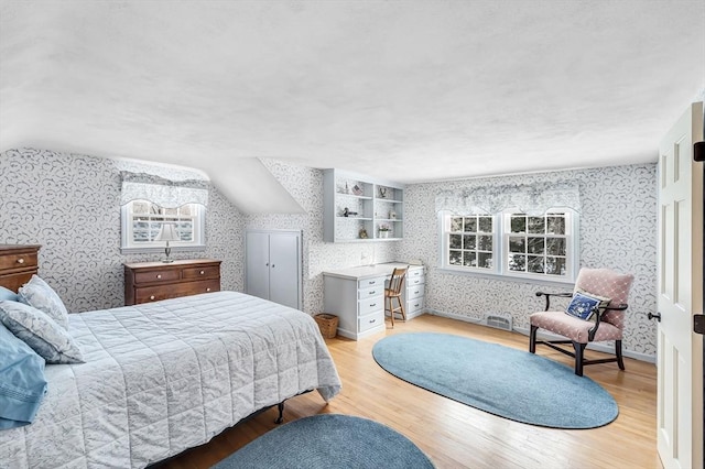 bedroom featuring light wood-type flooring, wallpapered walls, baseboards, and lofted ceiling