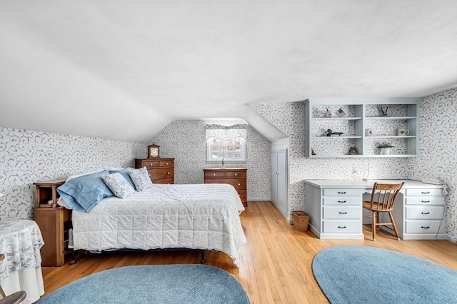 bedroom featuring vaulted ceiling, light wood-style flooring, and wallpapered walls