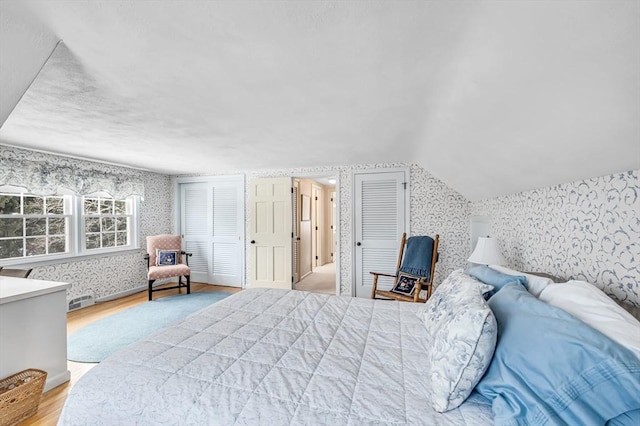 bedroom with lofted ceiling, wood finished floors, visible vents, multiple closets, and wallpapered walls