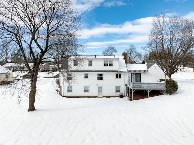 snow covered back of property featuring a chimney and a wooden deck