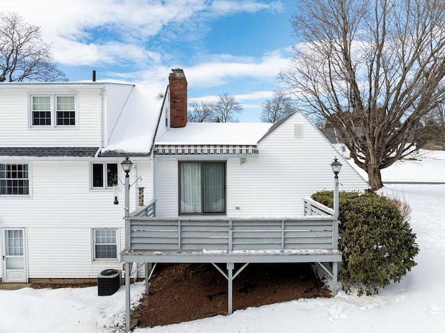 snow covered property featuring central AC unit, a chimney, and a wooden deck