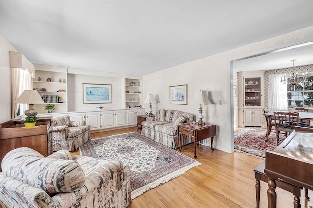 living area featuring light wood-style flooring, built in shelves, a chandelier, and baseboards