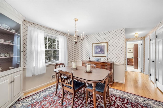 dining space featuring light wood-type flooring, wallpapered walls, baseboards, and a chandelier