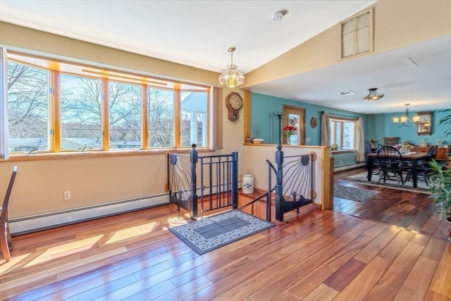 interior space featuring visible vents, vaulted ceiling, wood finished floors, a baseboard heating unit, and a notable chandelier