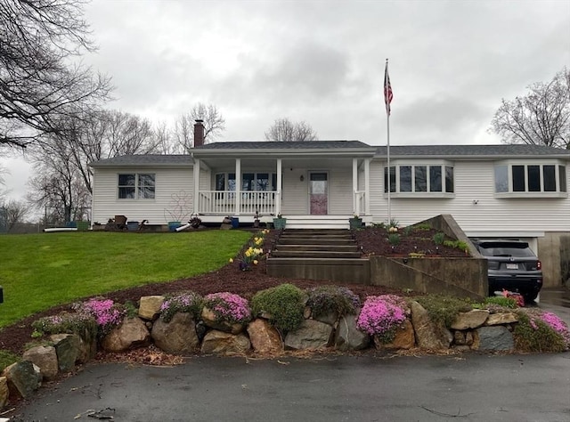 ranch-style home with covered porch, a garage, a chimney, and a front lawn