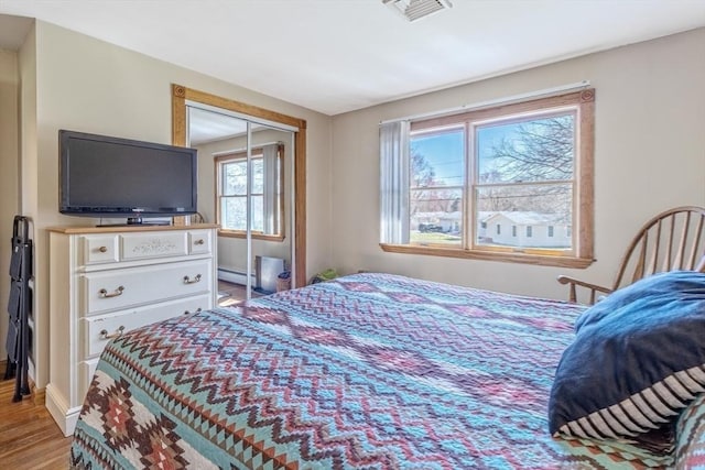 bedroom with visible vents, a closet, baseboards, a baseboard radiator, and light wood finished floors