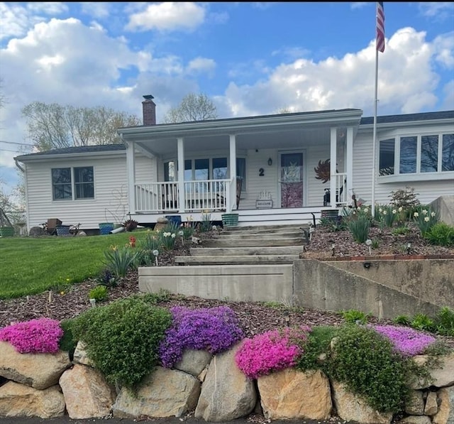 view of front of home with a front lawn, covered porch, and a chimney