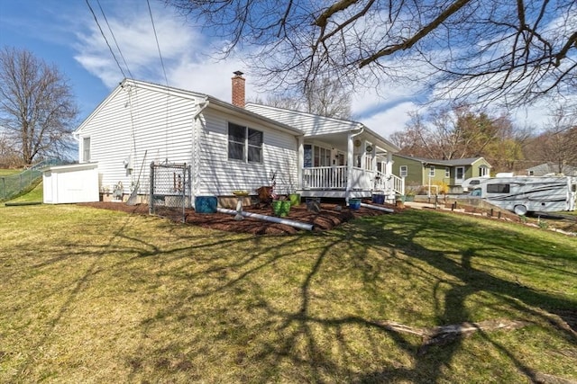 back of house with a porch, a yard, fence, and a chimney