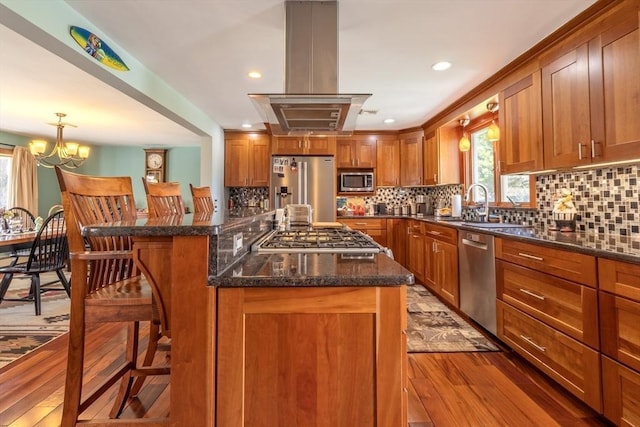 kitchen with a sink, a kitchen breakfast bar, stainless steel appliances, island range hood, and wood finished floors