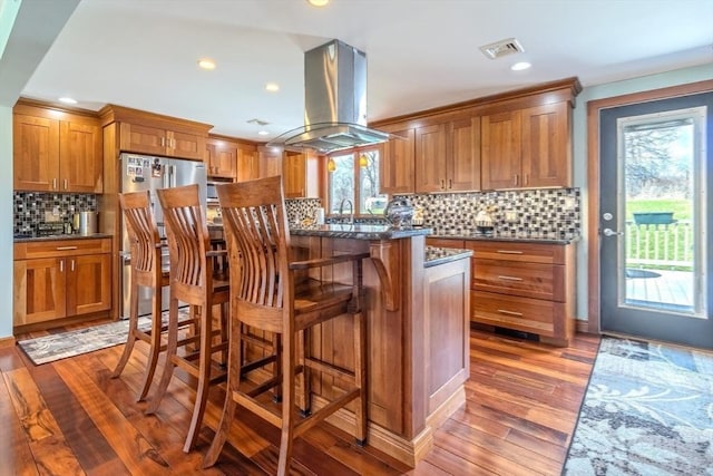kitchen featuring brown cabinets, a breakfast bar, light wood-style floors, island range hood, and backsplash