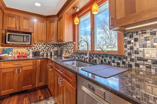 kitchen with brown cabinetry, a sink, dark stone countertops, and stainless steel microwave