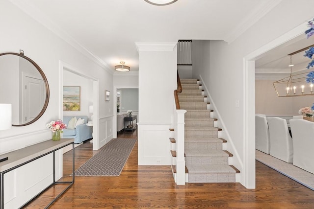 staircase featuring a decorative wall, crown molding, a wainscoted wall, wood finished floors, and a notable chandelier