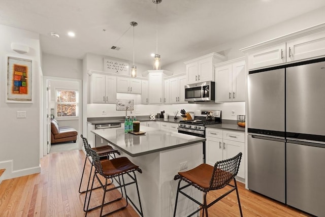kitchen with a kitchen bar, visible vents, dark countertops, light wood finished floors, and stainless steel appliances