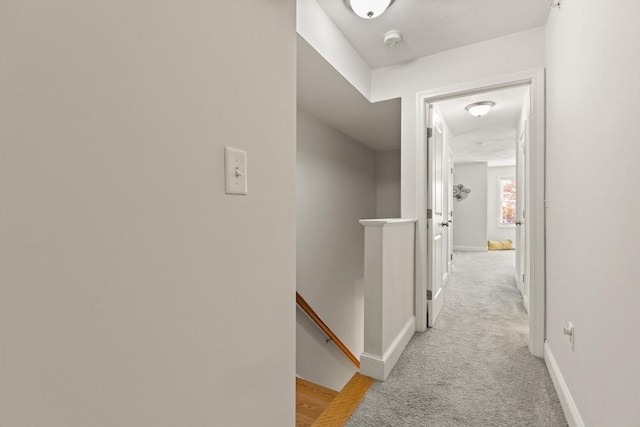hallway with baseboards, light carpet, and an upstairs landing