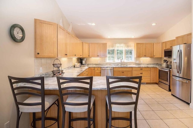 kitchen with a peninsula, light brown cabinets, appliances with stainless steel finishes, and light countertops